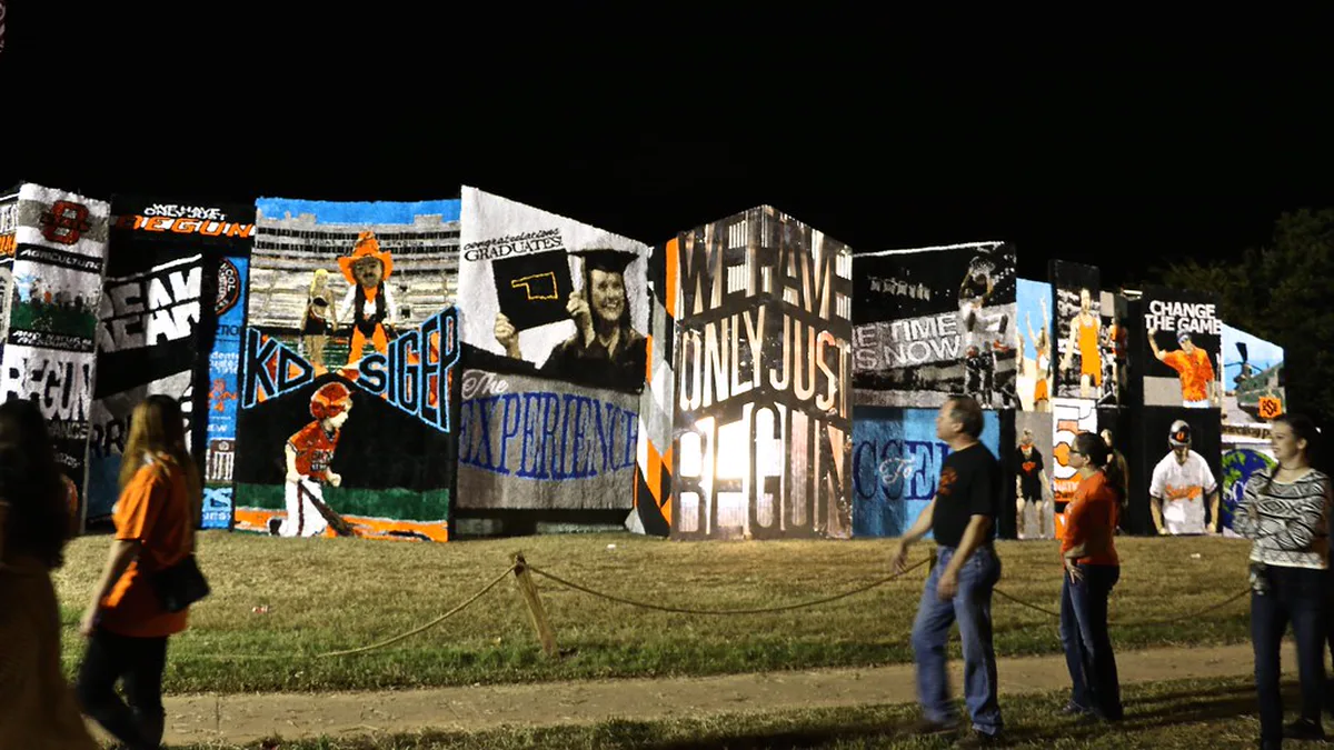 Campus Homecoming Pomp Displays Lit Up at Night Visitors walk past a row of large campus homecoming displays made of tissue paper pomps, lit at night on a university lawn