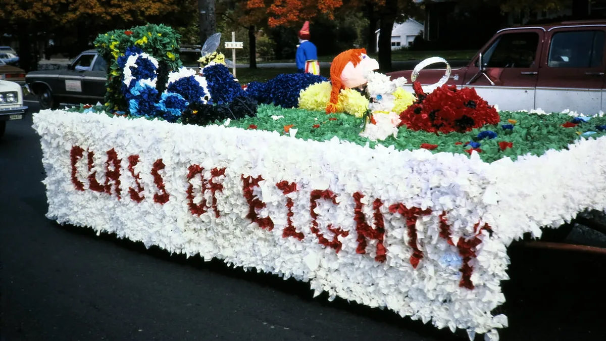 Class Homecoming Float Covered in White and Red Tissue Paper Pomps Homecoming float ideas in practice: a class float skirted in white tissue pomps with red letters and a flower garden on the deck