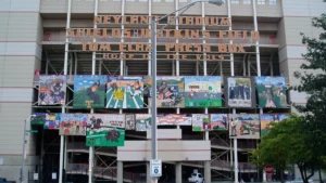 Two rows of hand-painted homecoming theme banners from student groups hanging across the front of a college football stadium