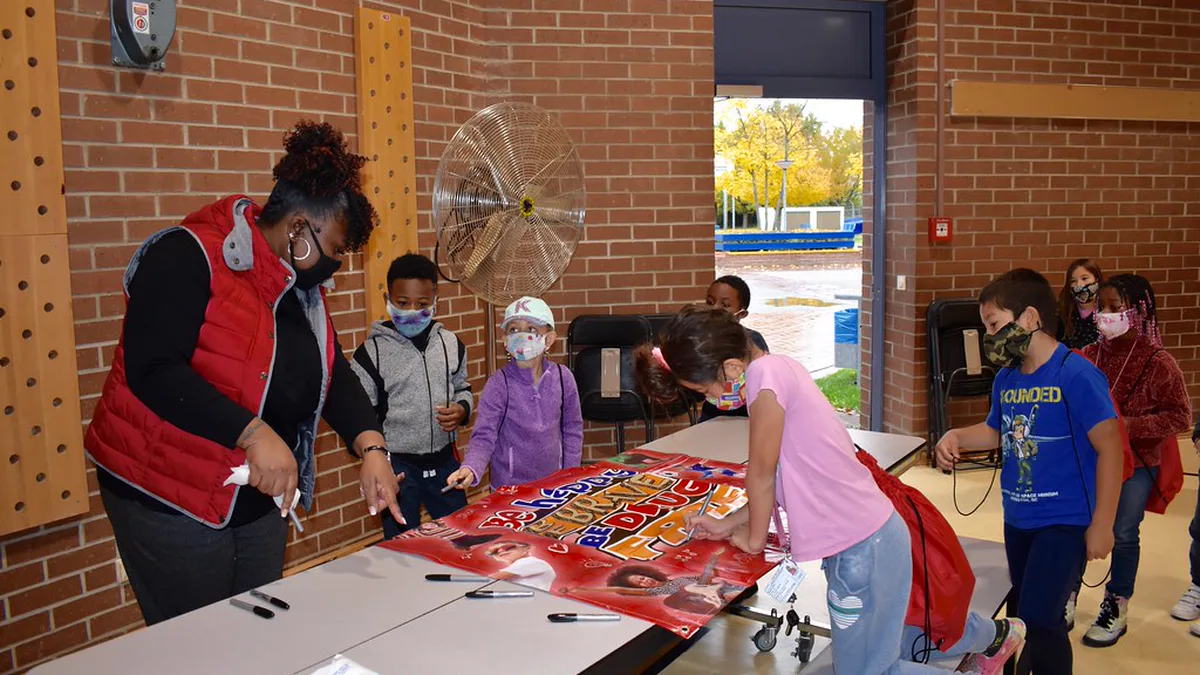 Students Signing a Drug Free Pledge Banner During Red Ribbon Week Students lining up at a cafeteria table to sign a red drug free pledge banner while a staff member hands out markers