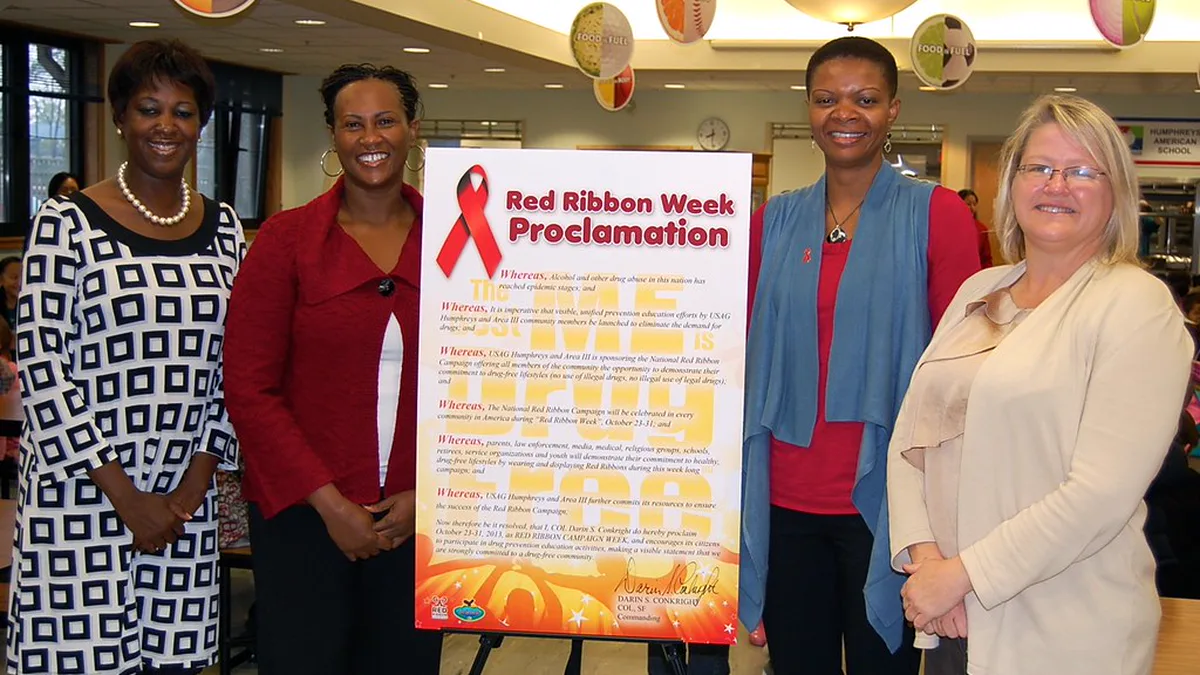 Red Ribbon Week Proclamation Poster Displayed in a School Cafeteria Staff members in red standing beside a large Red Ribbon Week proclamation poster on an easel in a school cafeteria