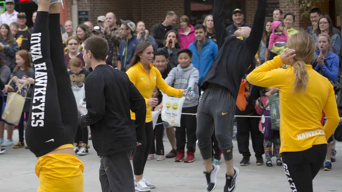 Campus Homecoming Parade With Spirit Squads in School Colors Spirit squad members in black and gold doing a handstand and jumping for a crowd lining a downtown street during a university homecoming parade