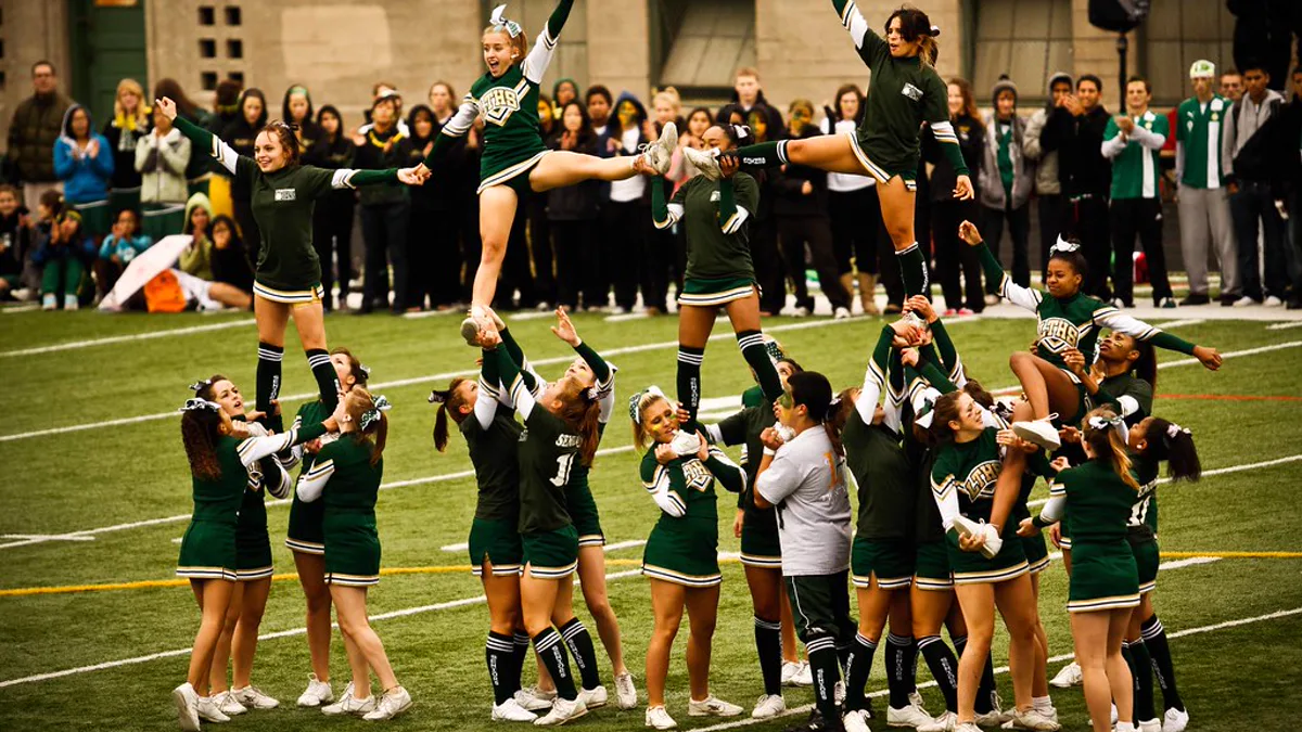 Spirit Squad Stunts on the Sideline at a High School Pep Rally High school cheer team in green and gold uniforms stunting on a turf field while a crowd in school colors watches a pep rally