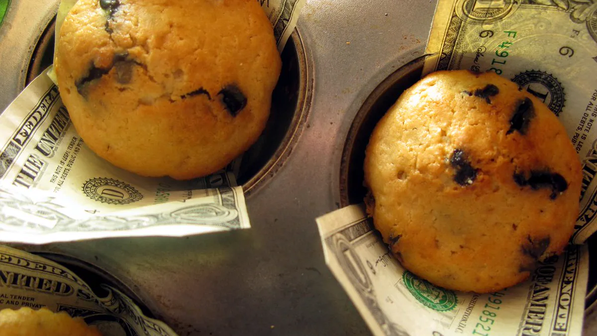 Bake Sale Muffins Sitting on Dollar Bills in a Muffin Tin Blueberry muffins in a metal muffin tin with folded one dollar bills tucked under them, a bake sale fundraiser theme