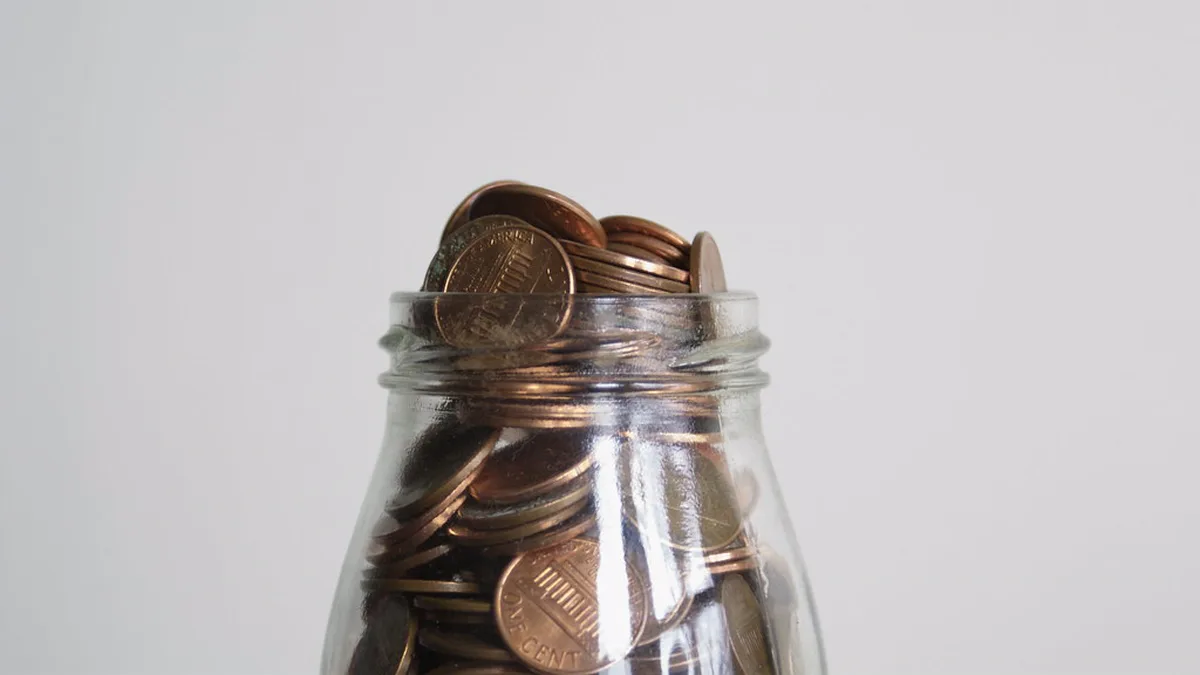 Glass Jar Filled With Pennies for a Penny War Glass jar packed with copper pennies against a plain gray wall, like the class jars used in a penny war fundraiser
